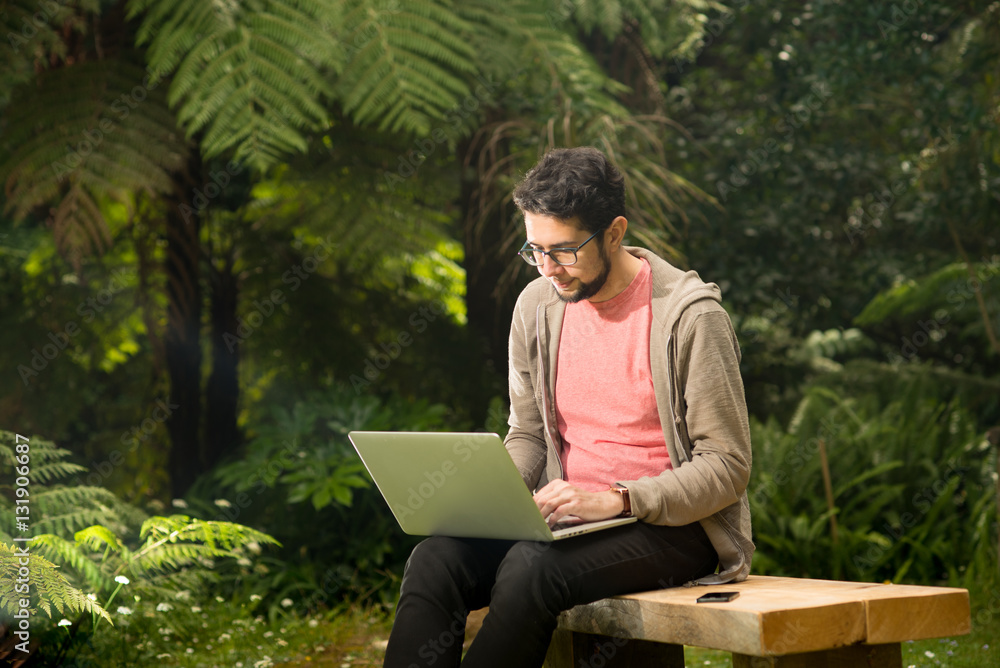 Young man with a laptop and smartphone sitting outdoor in a park