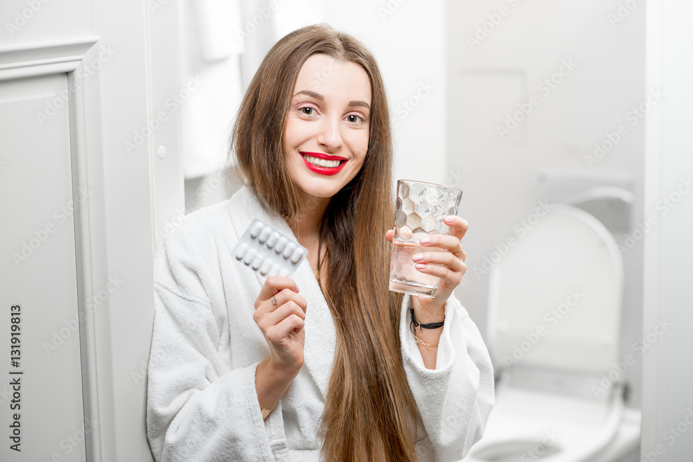 Smiling woman with pills and glass of water in the bathroom