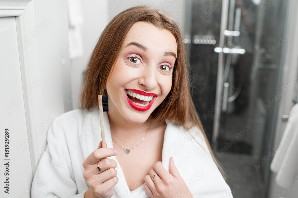 Close-up portrait of smiling woman in bathrobe with toothbrush in the bathroom. Healthy smile and or