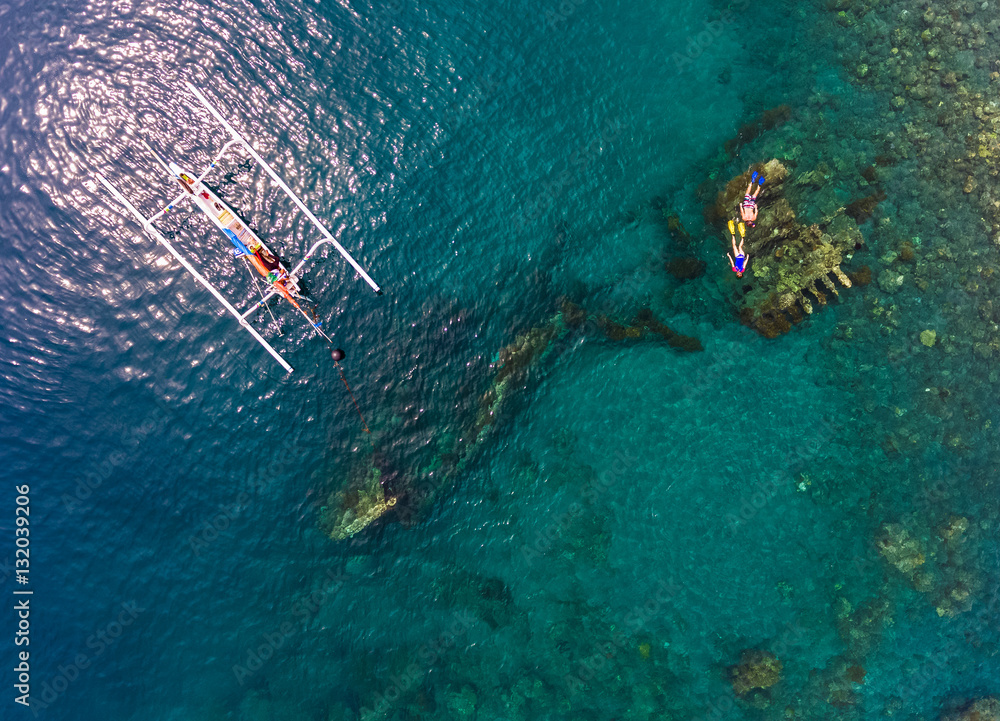 Aerial shot of the Japanese ship wreck with boat and people snorkeling over it. Bali, Indonesia