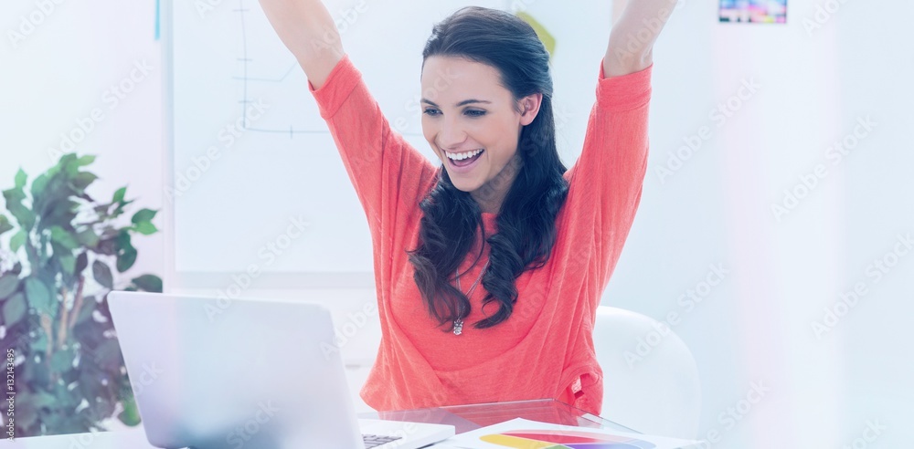 Excited woman raising her arms while working on her laptop