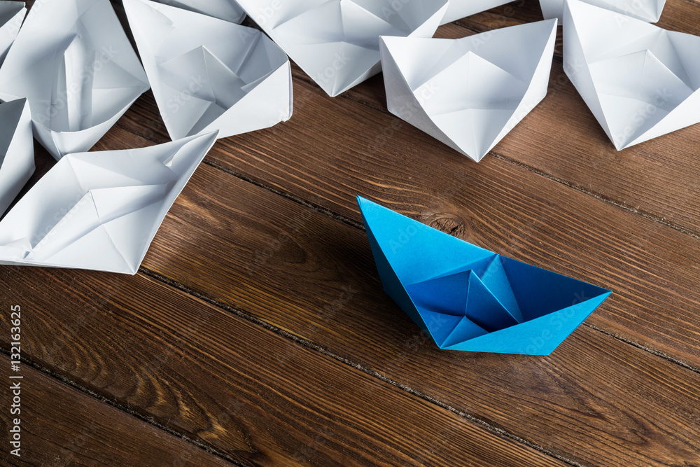 Business leadership concept with white and color paper boats on wooden table