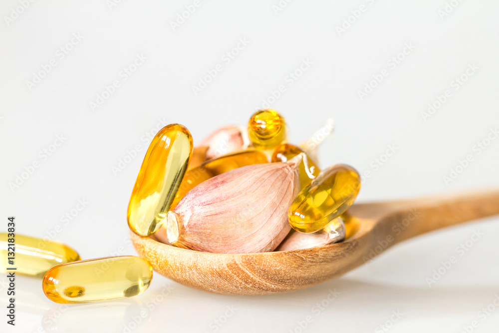 Close up garlic and oil capsule gel supplement in a wooden spoon