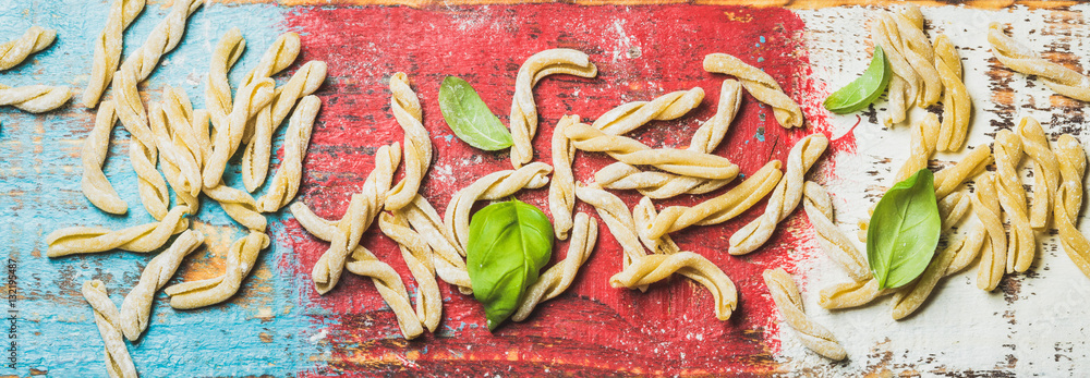 Homemade fresh uncooked Italian pasta casarecce with flour and green basil leaves on colorful painte