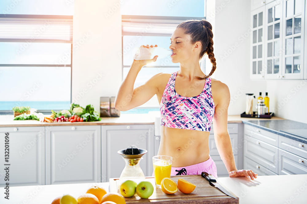 Athletic young female drinking water at kitchen