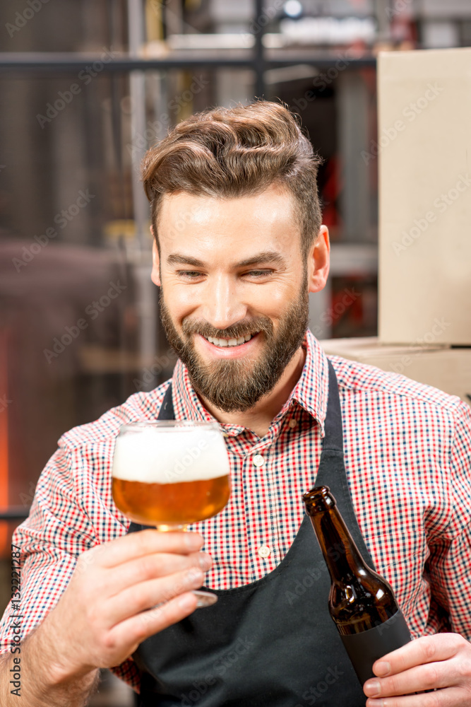 Handsome brewer expertising beer in the glass at the manufacturing