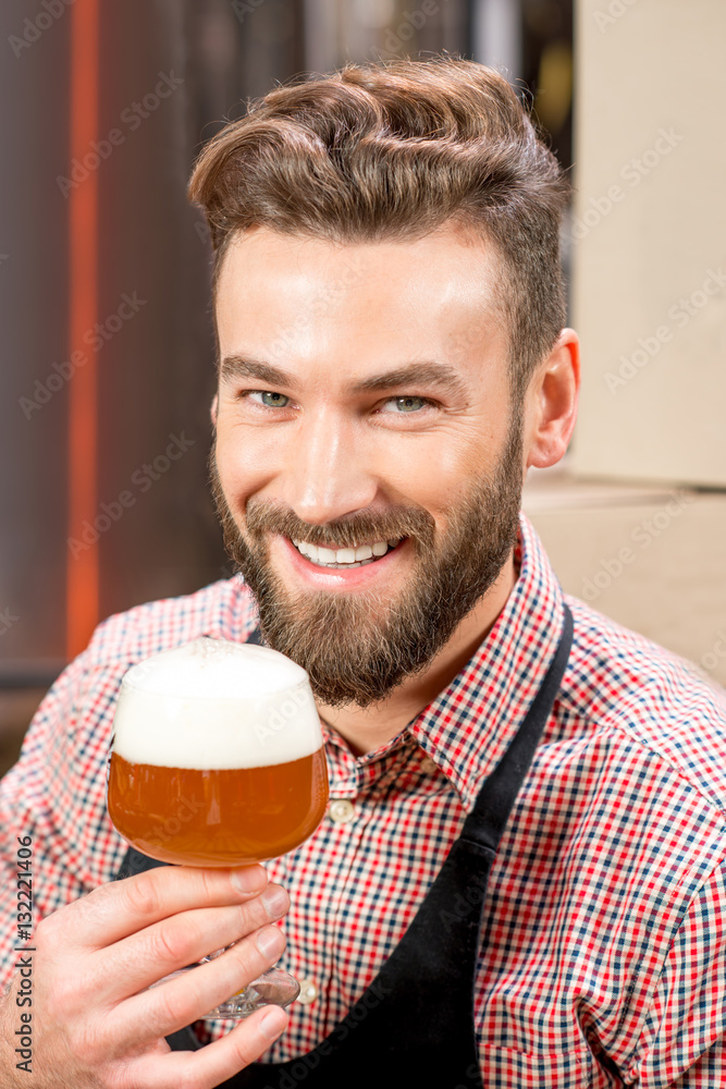 Close-up portrait of handsome brewer tasting beer in the glass