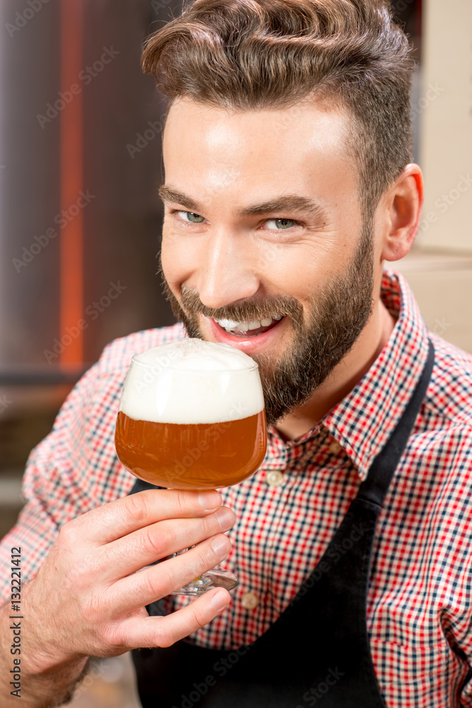 Close-up portrait of handsome brewer tasting beer in the glass