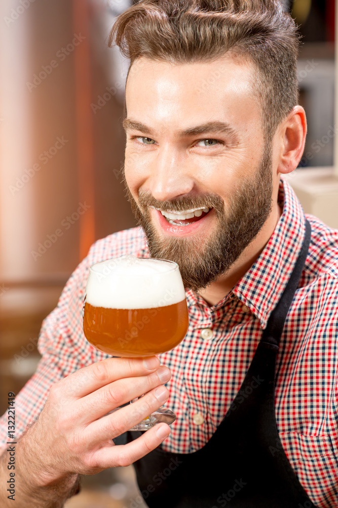 Close-up portrait of handsome brewer tasting beer in the glass