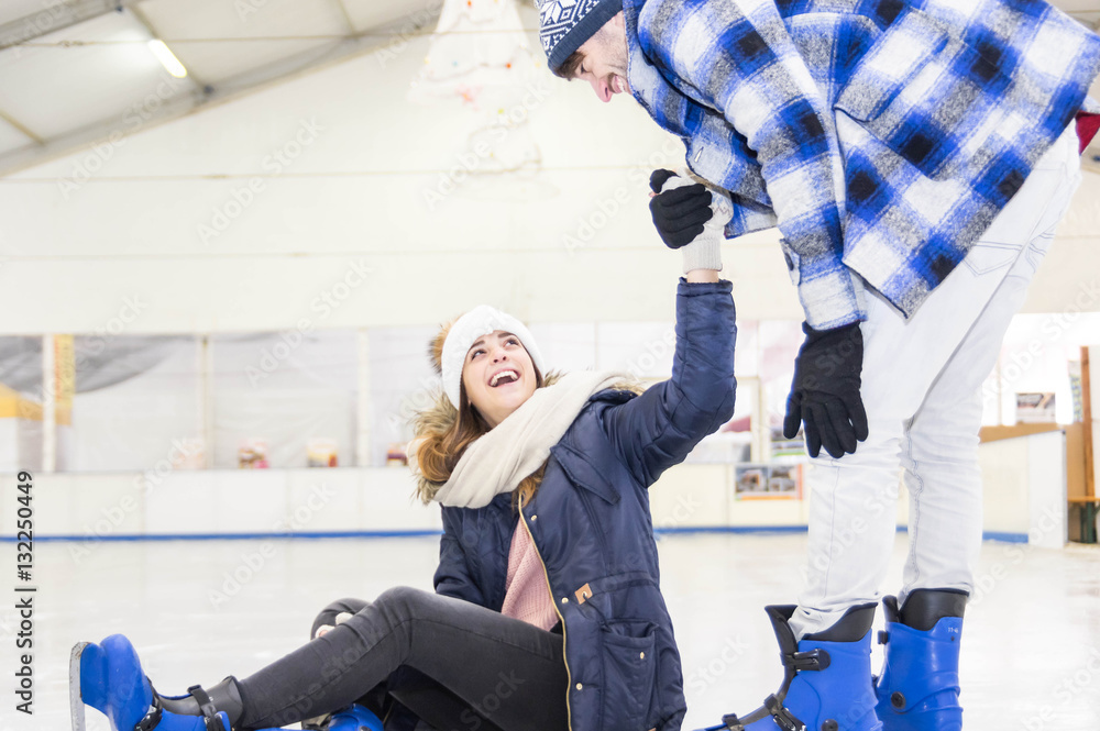 Smiling man helping women to rise up on skating rink.