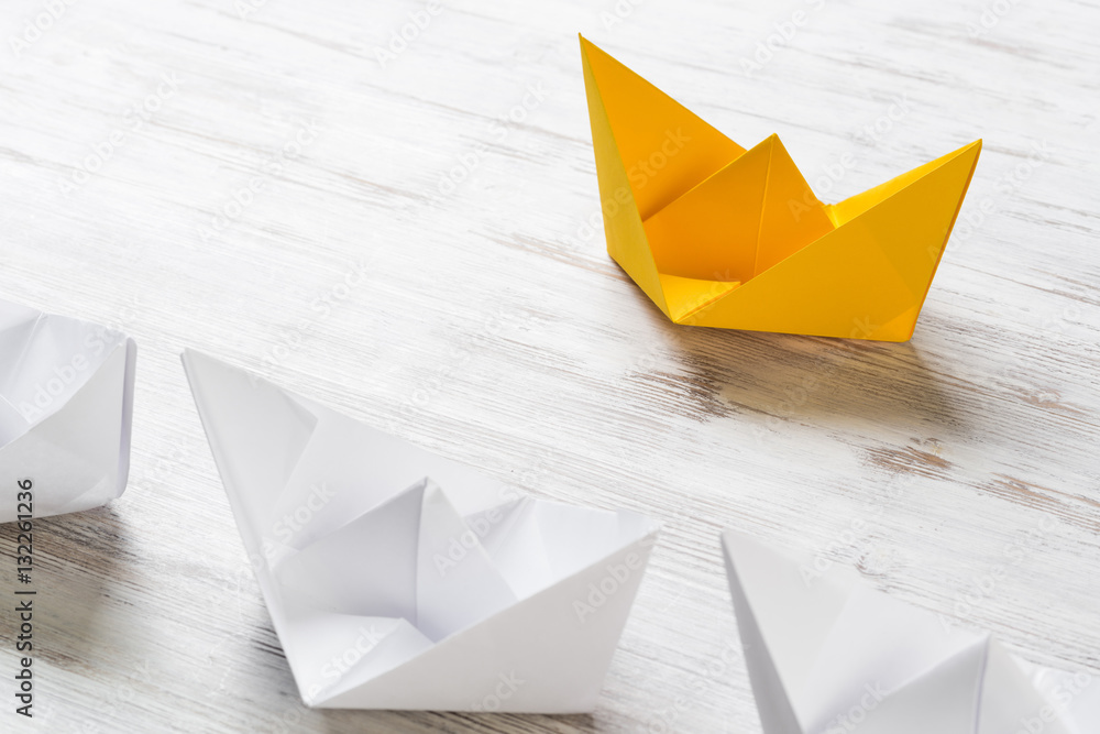 Business leadership concept with white and color paper boats on wooden table