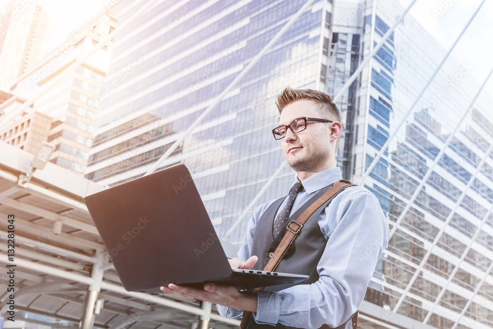 Young handsome businessman standing with laptop in the big city