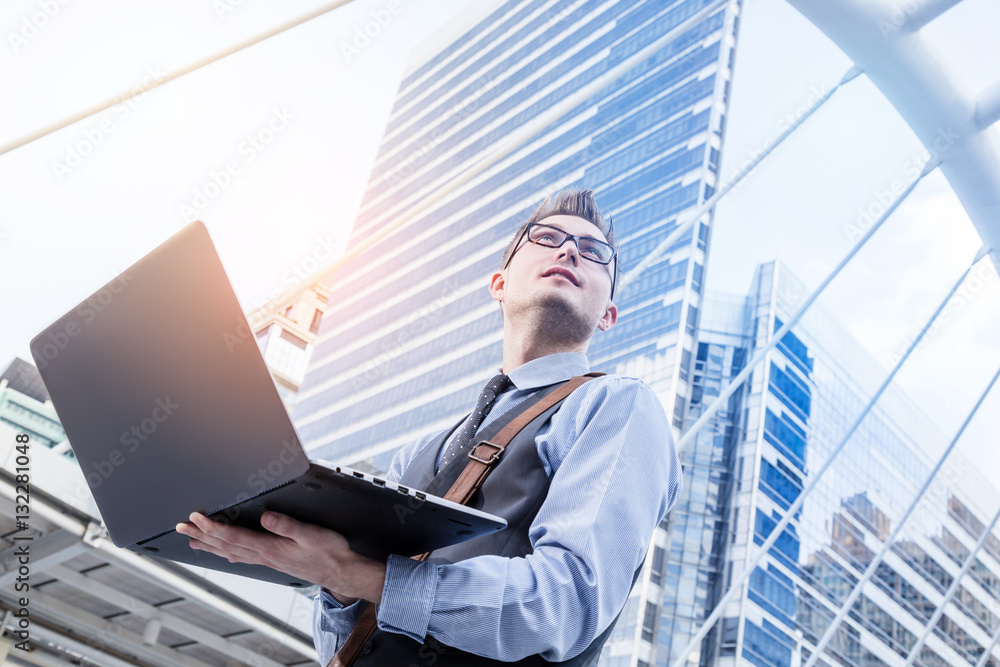 Young handsome businessman standing with laptop in the big city