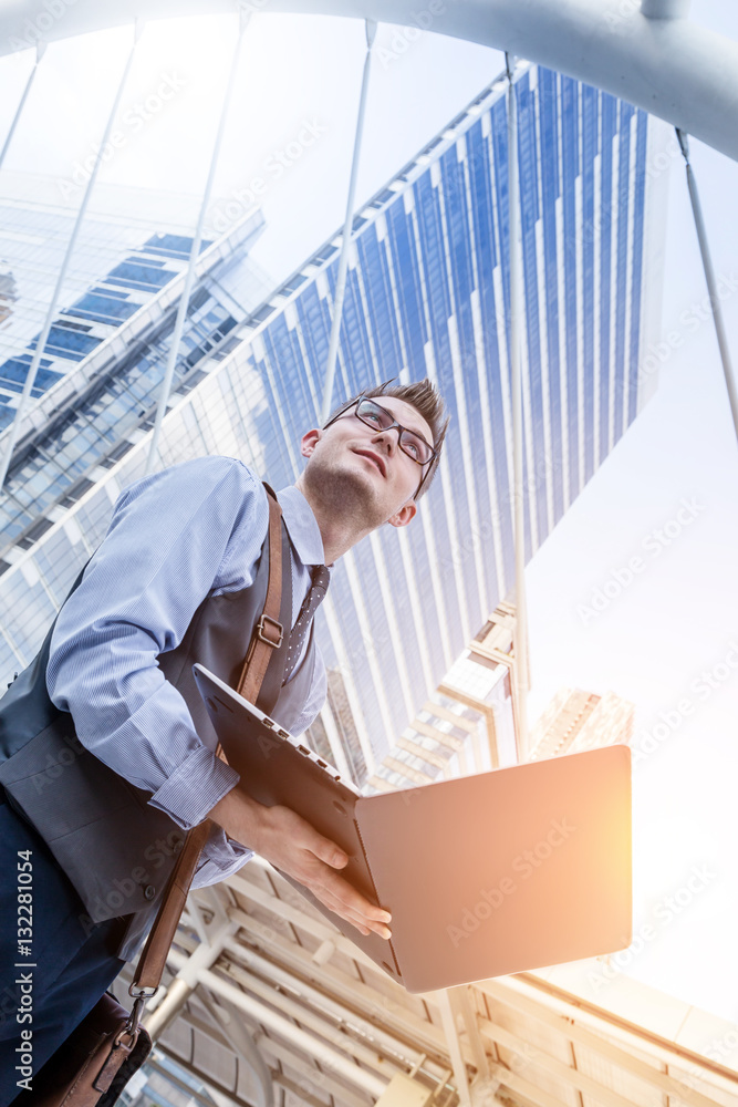 Young handsome businessman standing with laptop in the big city