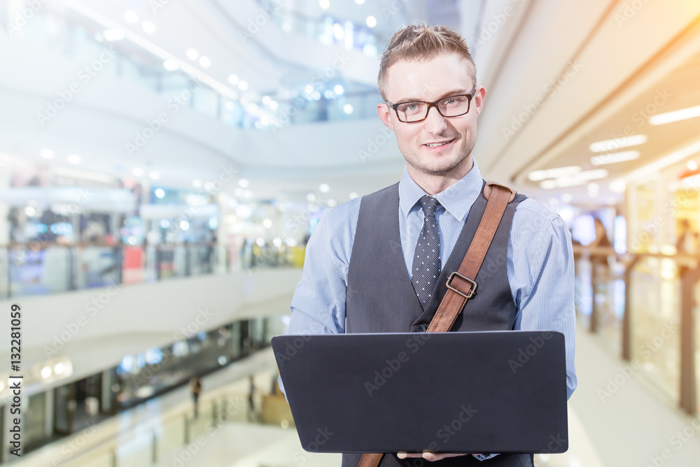 Young handsome businessman standing with laptop in the big city