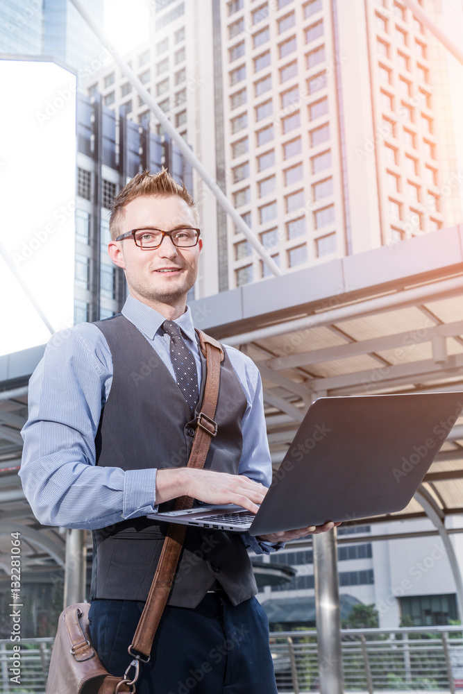 Young handsome businessman standing with laptop in the big city