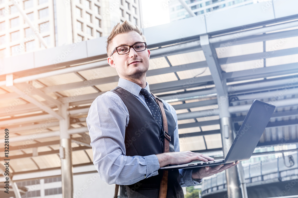 Young handsome businessman standing with laptop in the big city