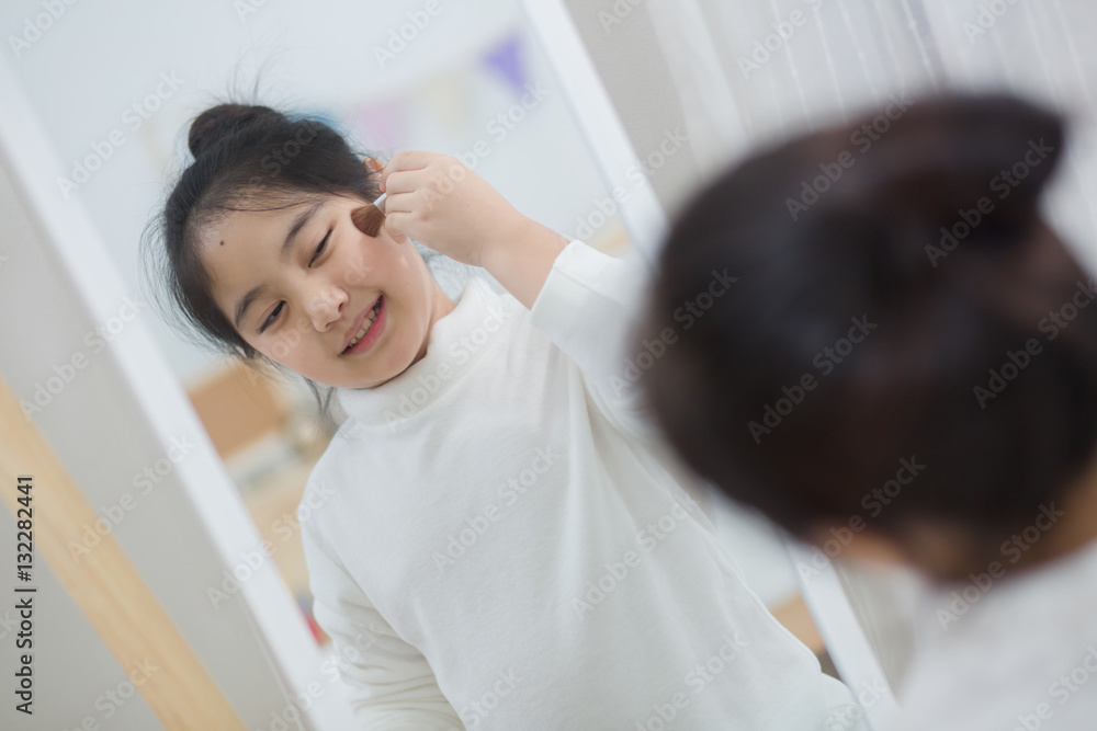 Pretty Asian child doing make up front of the mirror