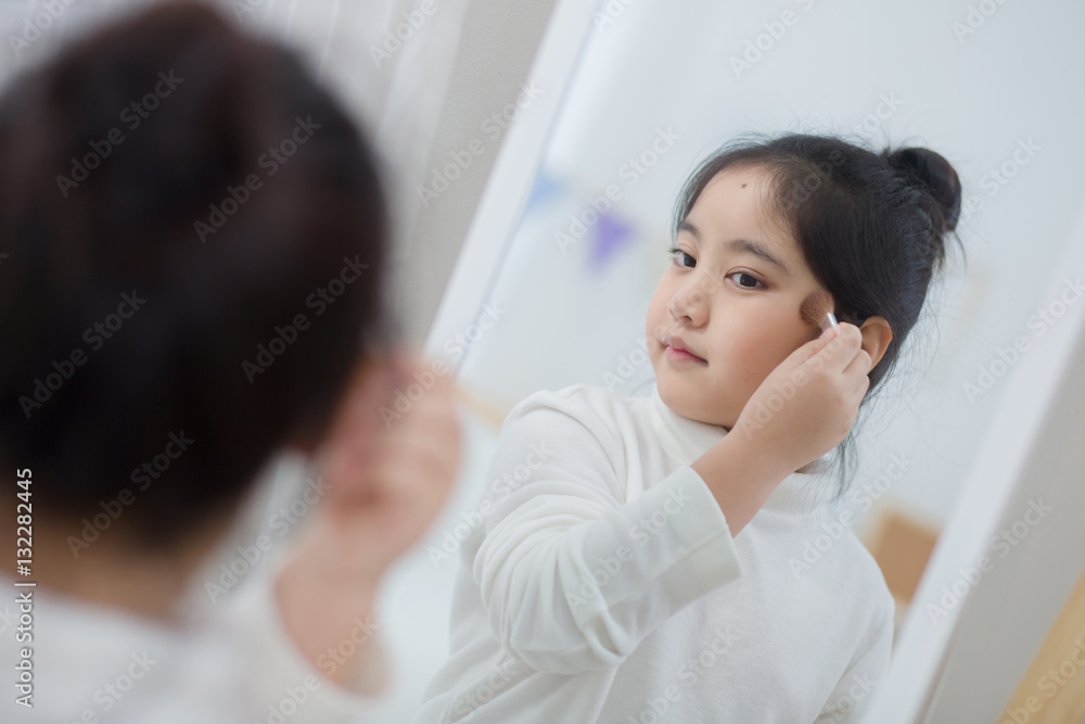 Pretty Asian child doing make up front of the mirror