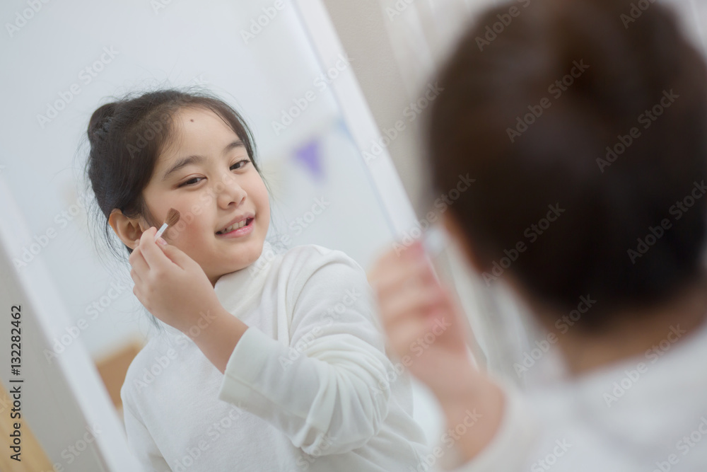 Pretty Asian child doing make up front of the mirror