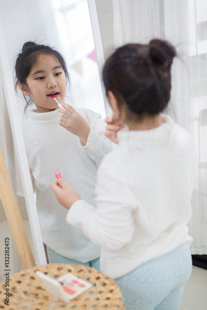 Pretty Asian child doing make up front of the mirror