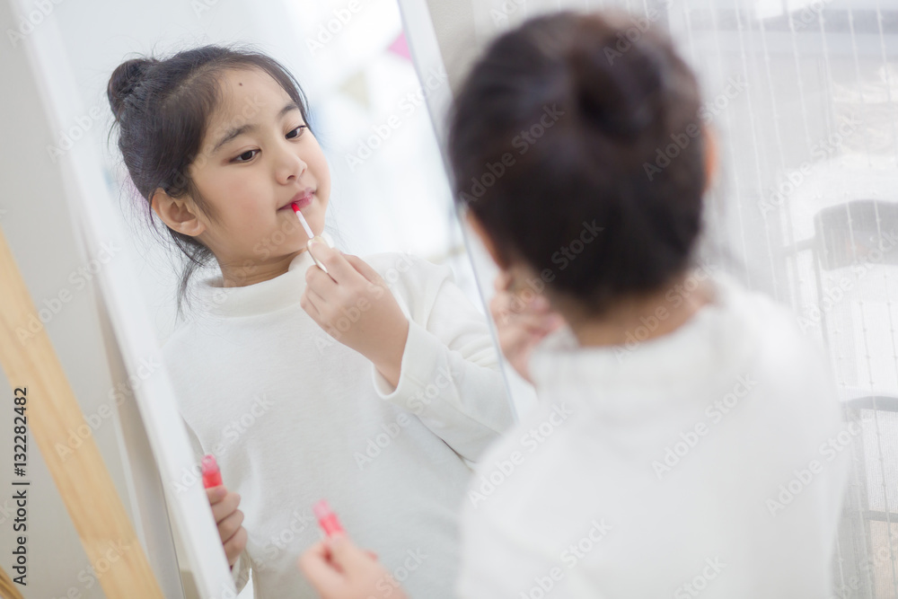 Pretty Asian child doing make up front of the mirror