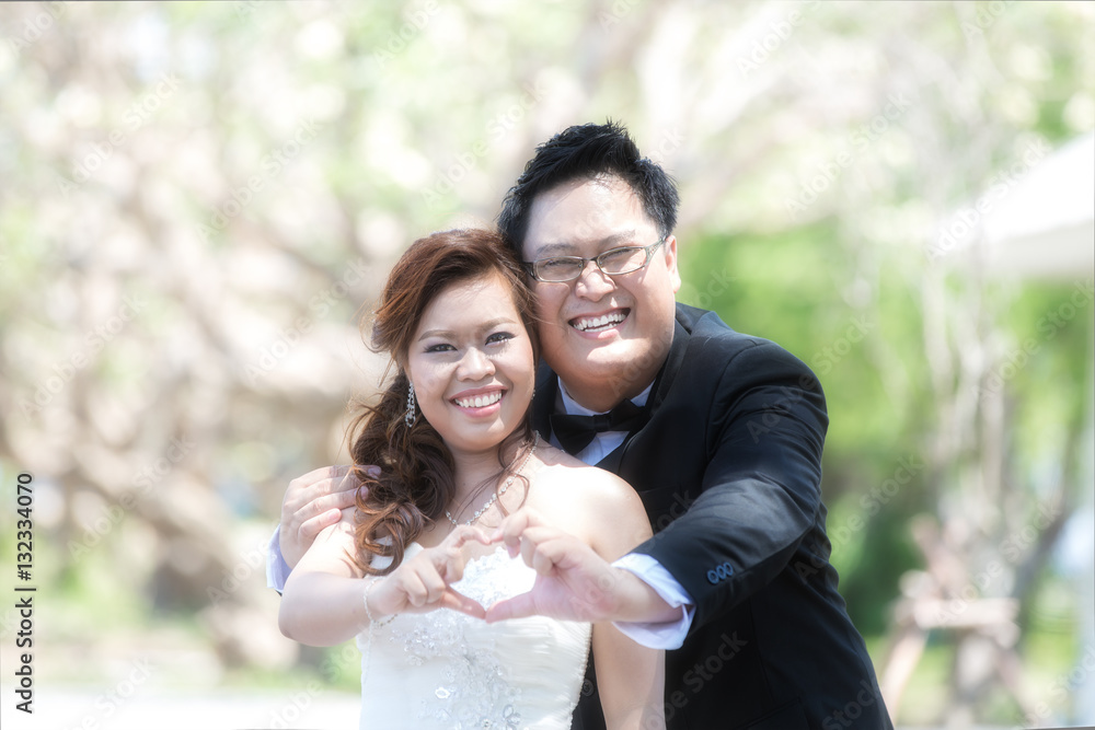 Portrait of cheerful wedding couple hugging and showing heart sh