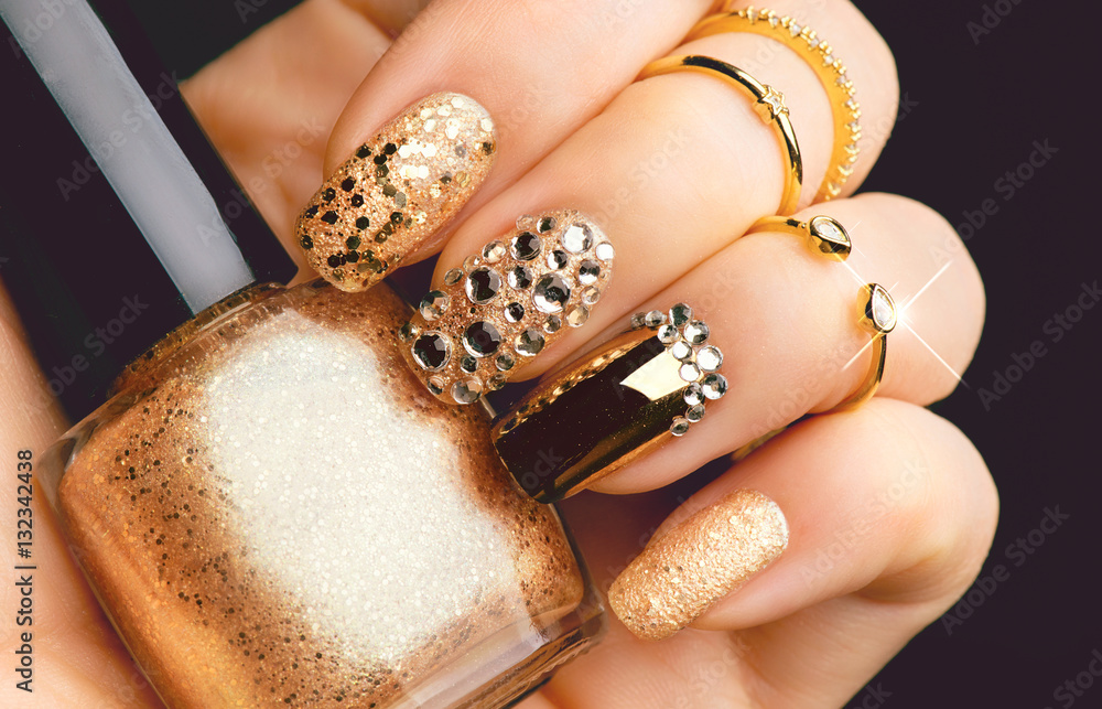 Golden nail art manicure. Holiday style bright manicure with gems and sparkles. Bottle of nail Polis