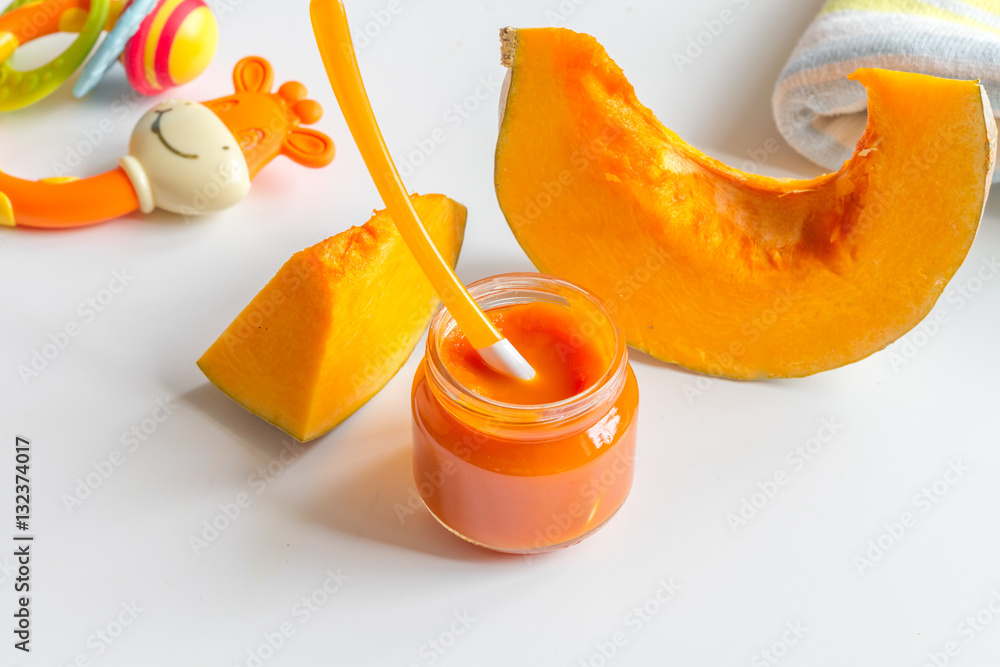 baby mashed with spoon in glass jar on white background