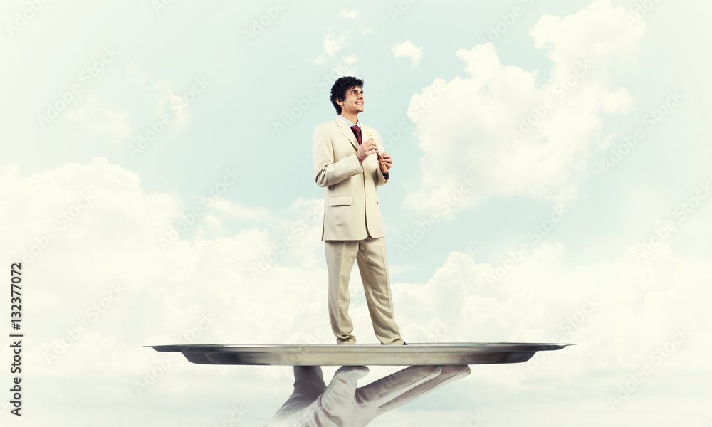 Businessman on metal tray playing fife against blue sky background