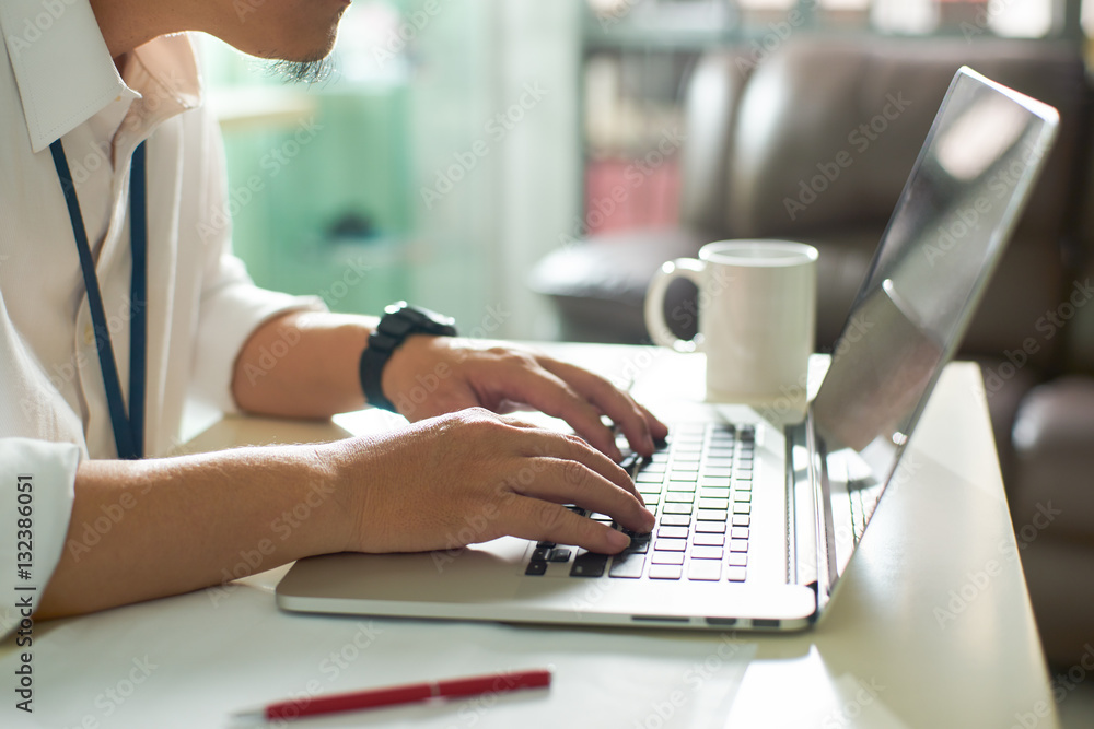 Businessman using laptop with tablet and pen on white table in office with a cup of coffee,side view