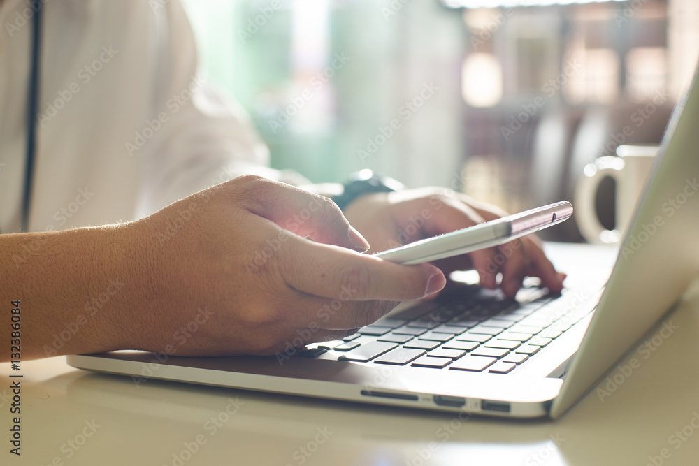 businessman hand using smart phone and keying the data to laptop,close up Seleted focus.