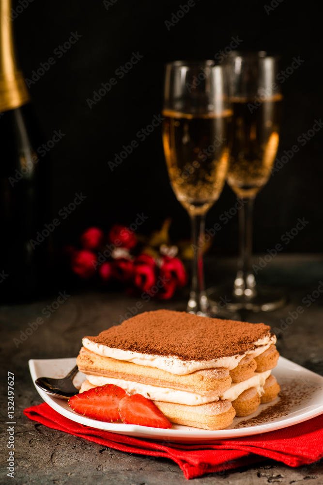 Tiramisu with strawberry and glasses of champagne on the table. Valentines concept. Dark moody style