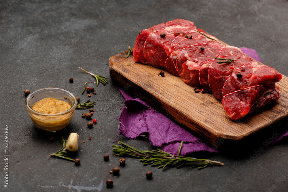 木板上的生肉配香料、芥末和迷迭香。新鲜牛肉。烤。准备烤。T