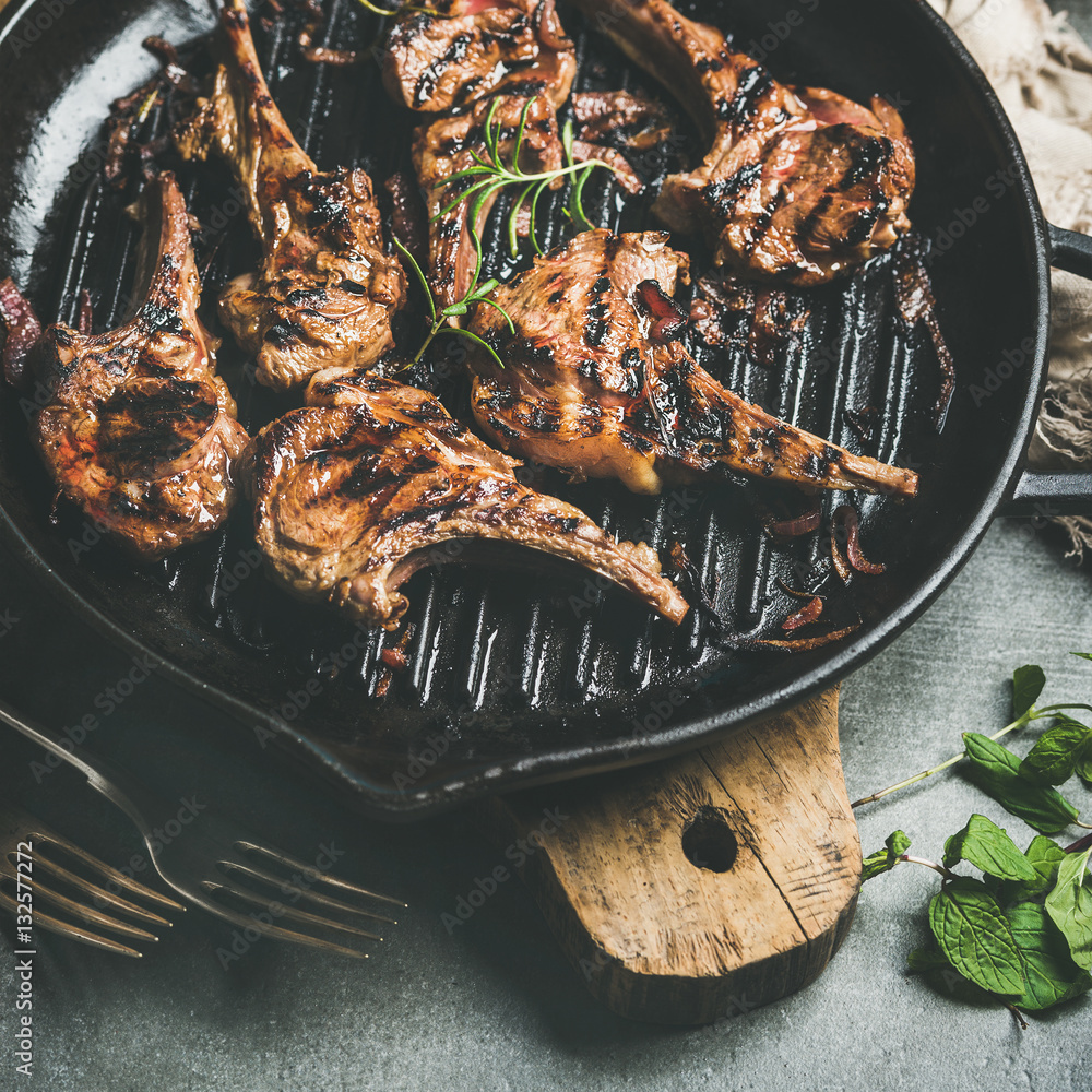 Barbecue dinner. Close-up of grilled lamb meat chops with onion and rosemary in cast iron pan on woo