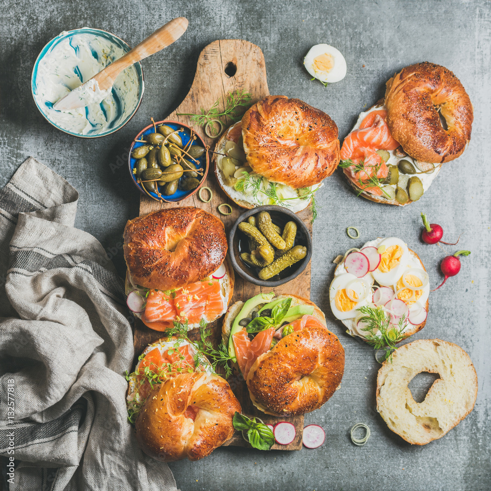 Variety of bagels with smoked salmon, eggs, radish, avocado, cucumber, greens and cream cheese in bo