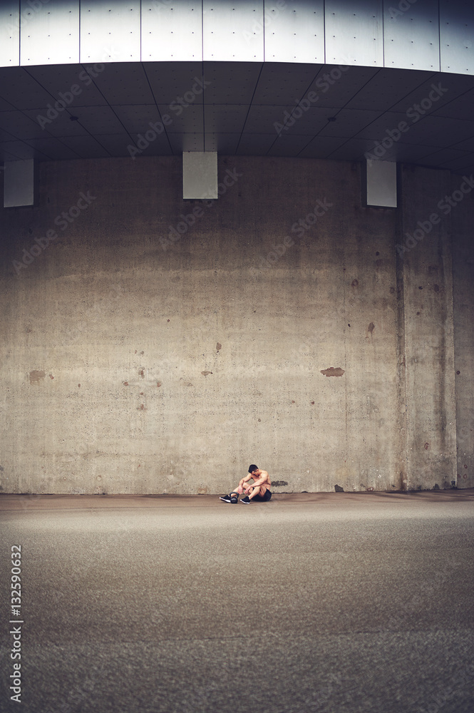 Distance shot man sitting against concrete wall