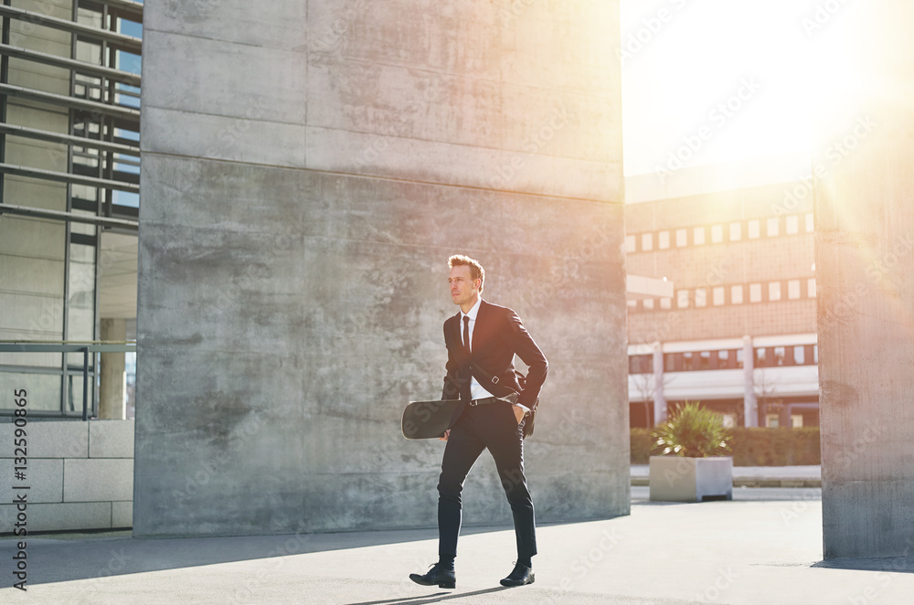 A businessman carries a skateboard in downtown