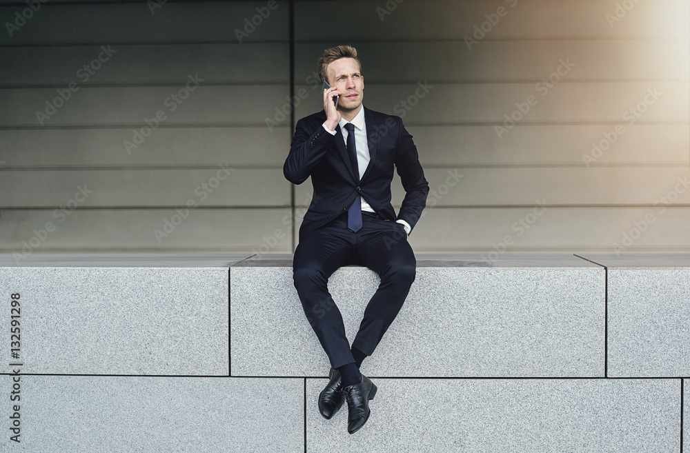 A businessman with legs crossed speaks phone