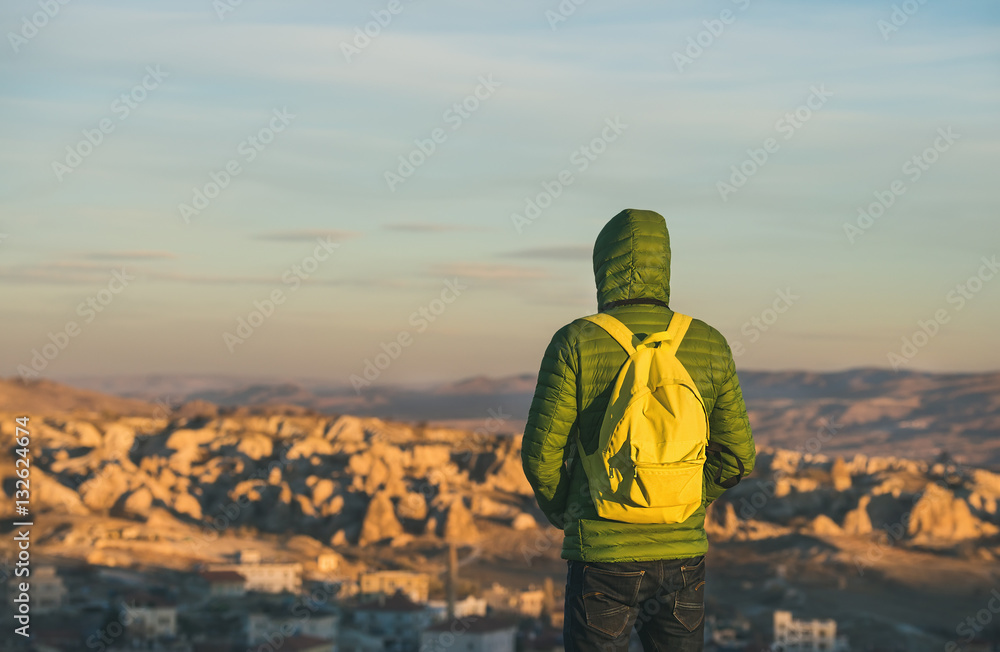 Young man traveller wearing bright clothing and yellow backpack standing and watching sunrise in the