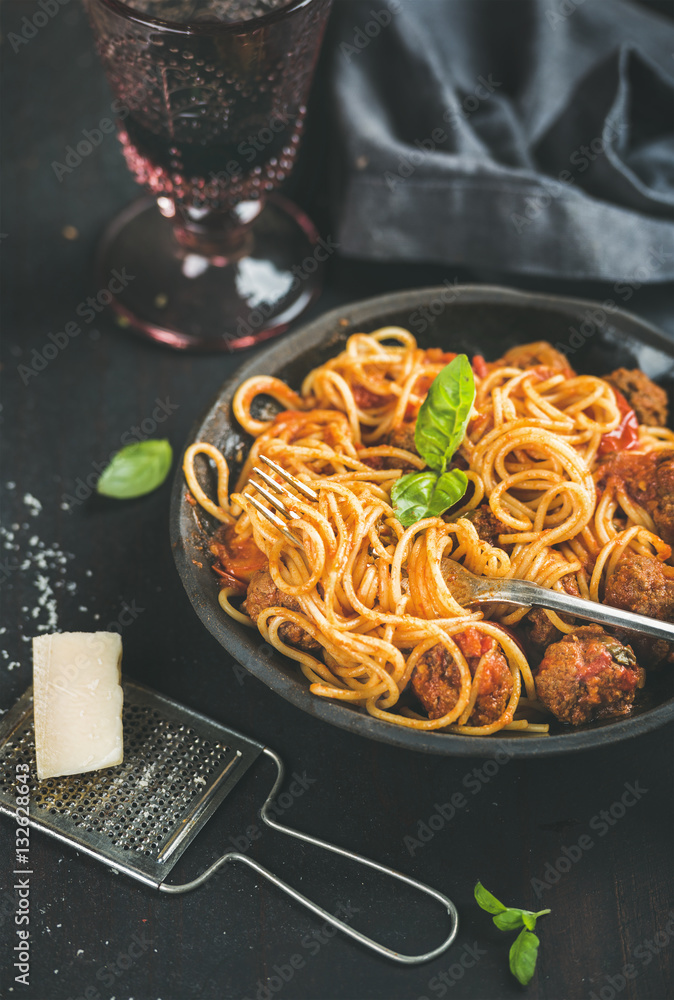 Italian pasta dinner. Spaghetti with meatballas, basil leaves and parmesan cheese in dark plate and 