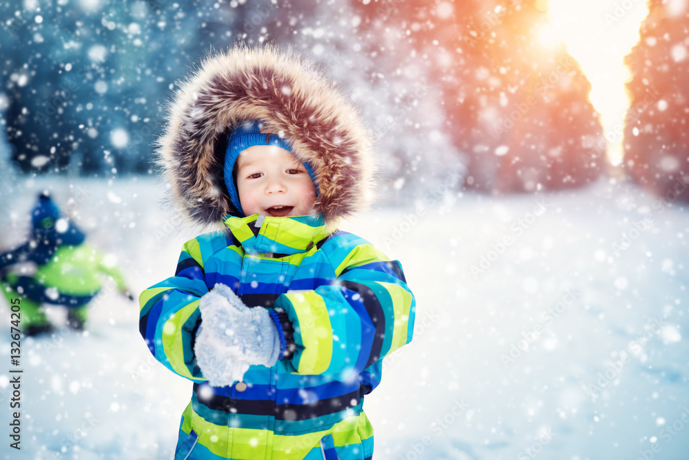 Boy in knitted hat, gloves and scarf outdoors at snowfall