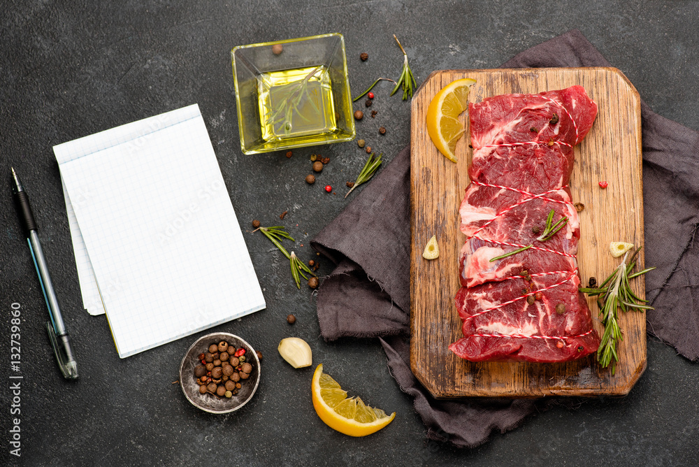 Raw meat with spices, lemon, olive oil and rosemary on wooden board. Recipe notebook. Fresh beef. Ro