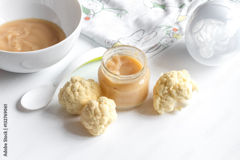 baby mashed with spoon in glass jar on white background