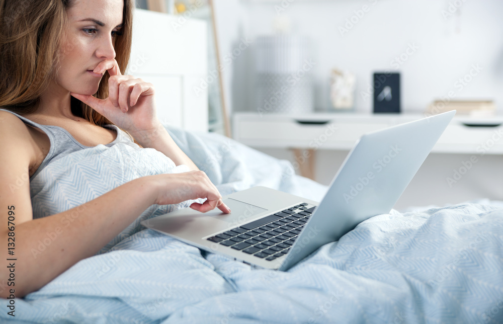 Young girl with laptop checking social media in bed at home