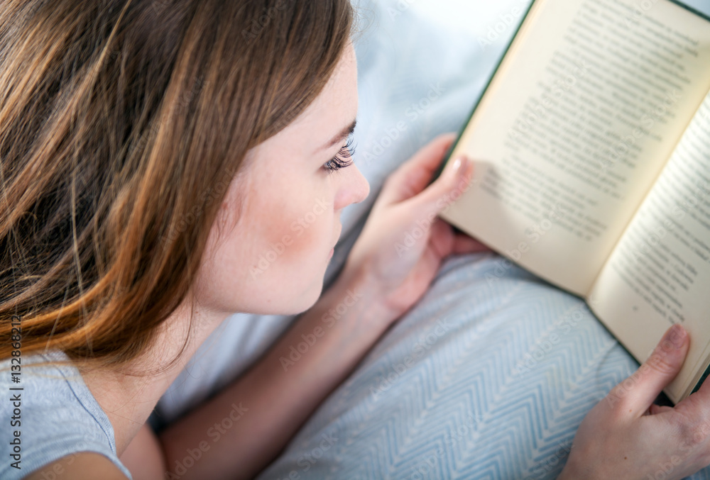 Girl reading book in bed at home