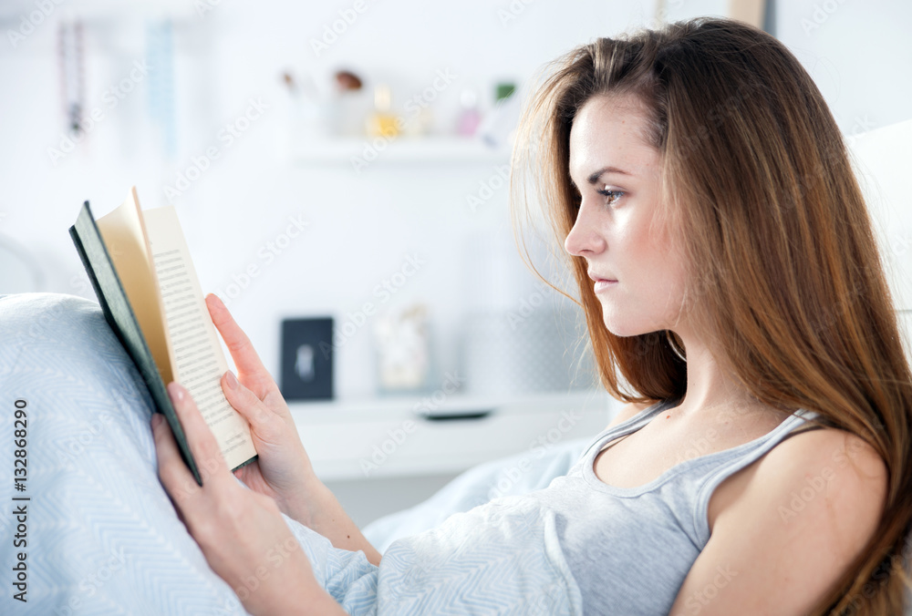 Girl reading book in bed at home