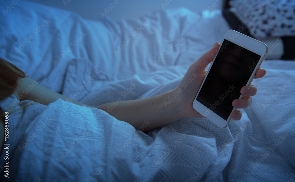 Girl in bed holding smart phone at night close up, blank screen