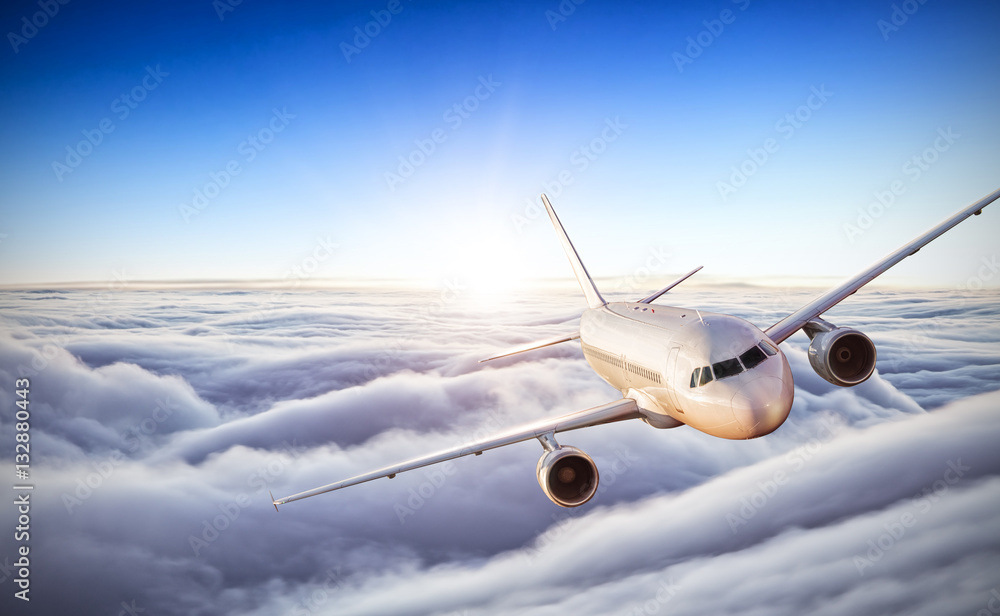 Airplane flying above clouds in dramatic sunset