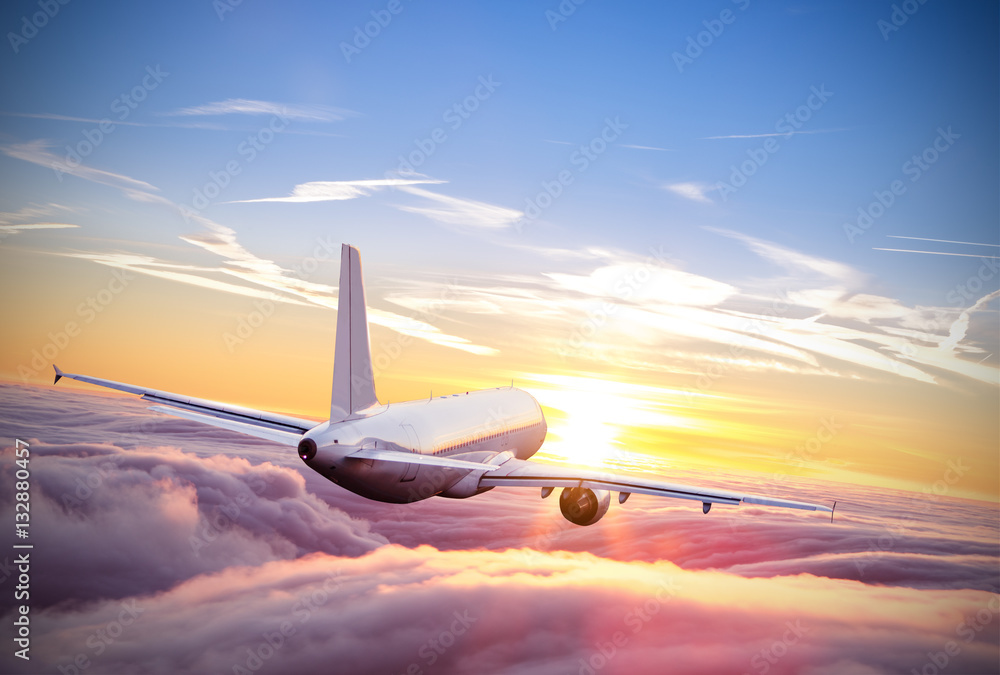 Airplane flying above clouds in dramatic sunset